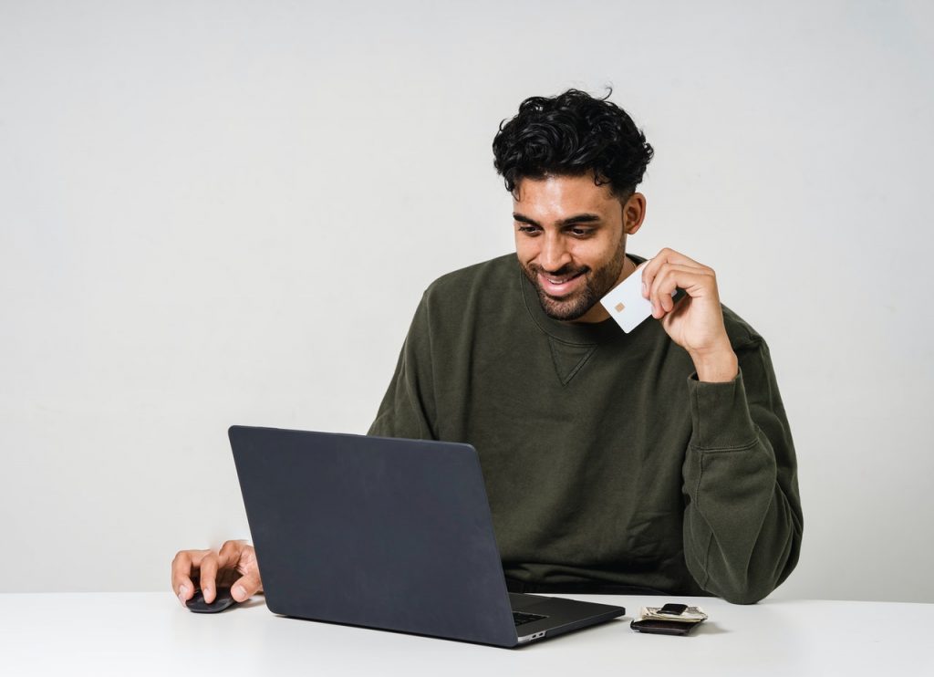 La foto de hombre usando un ordenador portátil con una tarjeta de crédito en la mano.